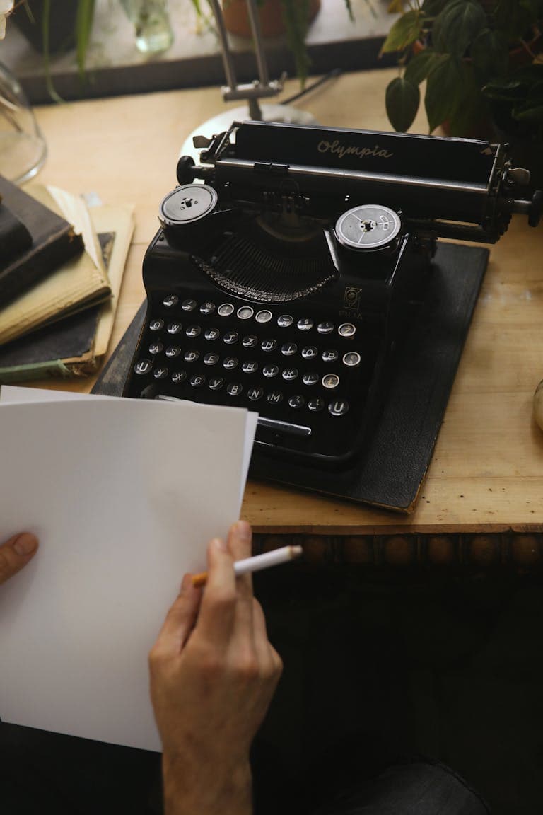 Vintage Olympia typewriter on wooden desk with green plant in background.