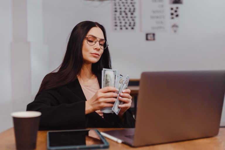 Woman handling cash and working on a laptop, emphasizing financial success and hard work.