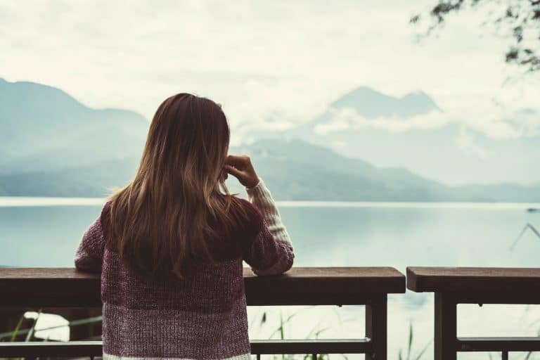 Woman with long hair gazing at foggy mountain lake from wooden deck, reflecting on life change